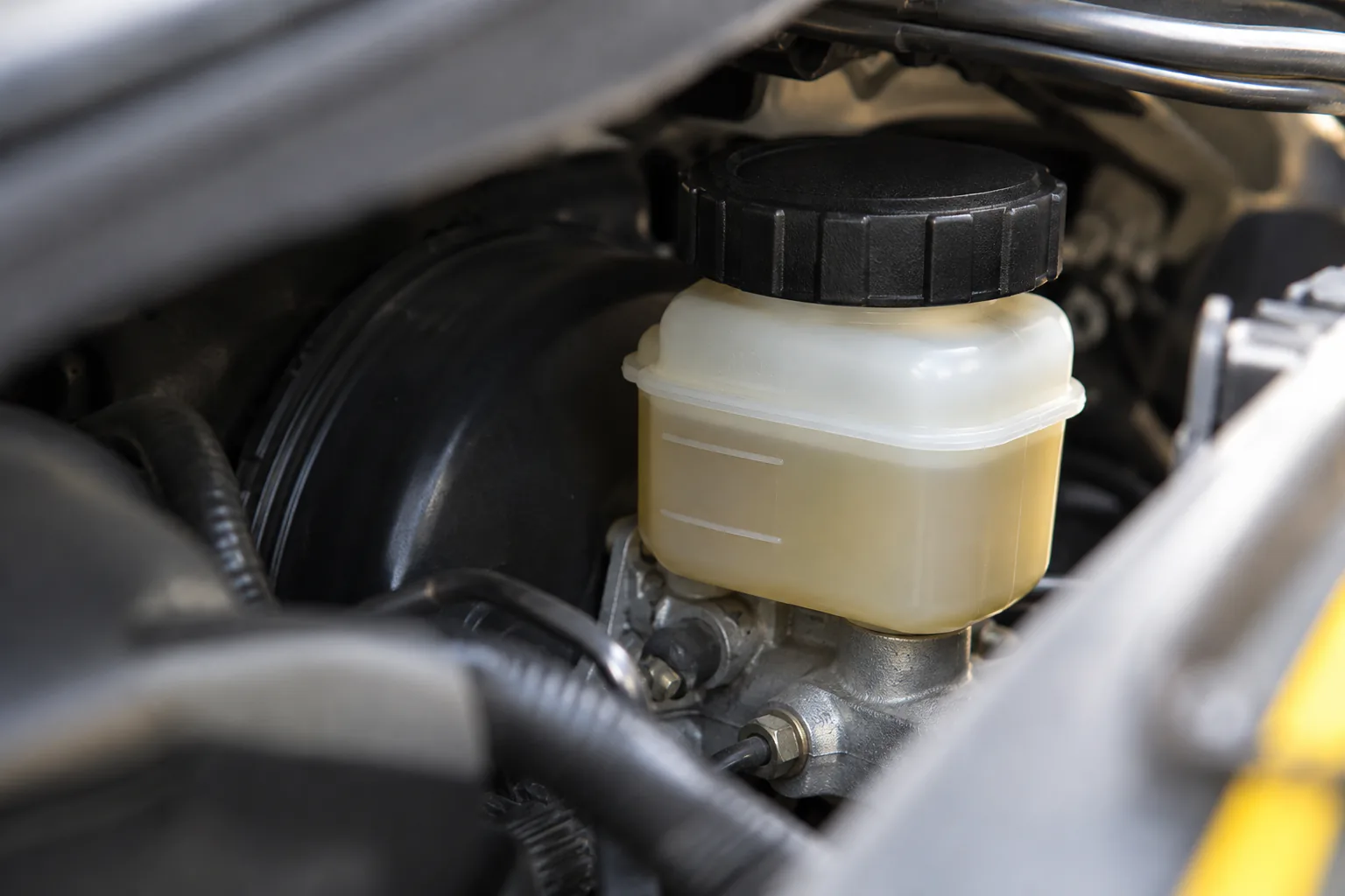 Close view of brake-fluid reservoir through engine-bay gap, cap intact, inspection light outside