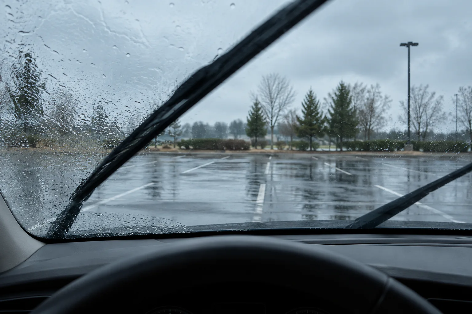 First-person interior view through evenly wet glass as blades sweep, open parking area ahead