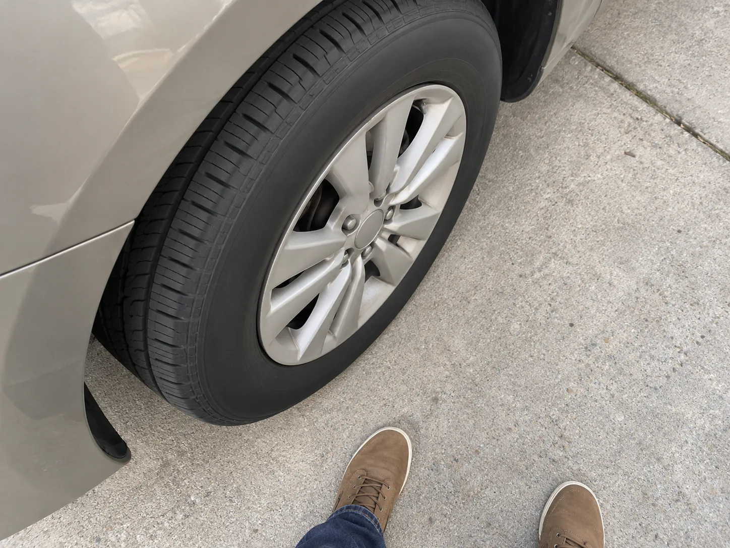 High-angle view beside front wheel showing full visible sidewall and pavement behind it, owner shoes safely outside roll path