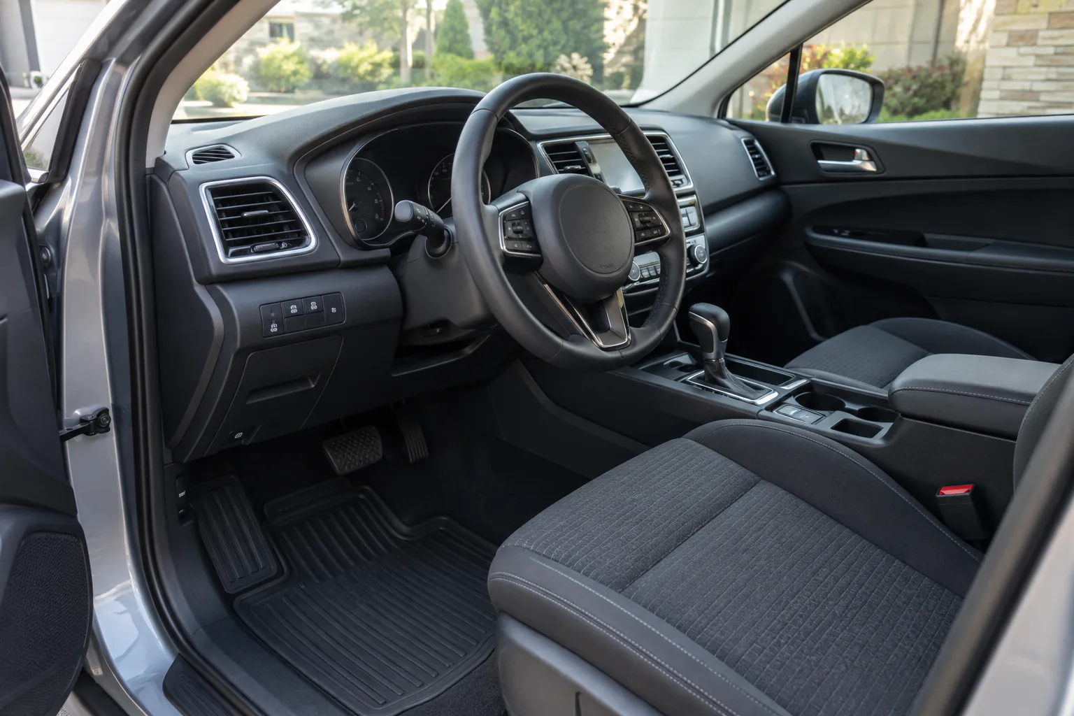 First-person view from an open driver's door toward the instrument cluster, floor mat, and windshield, with hands absent